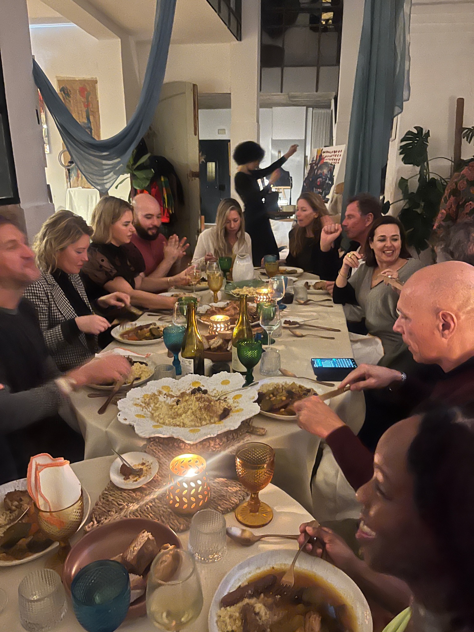 Guests smiling and eating together at a long candlelit table.